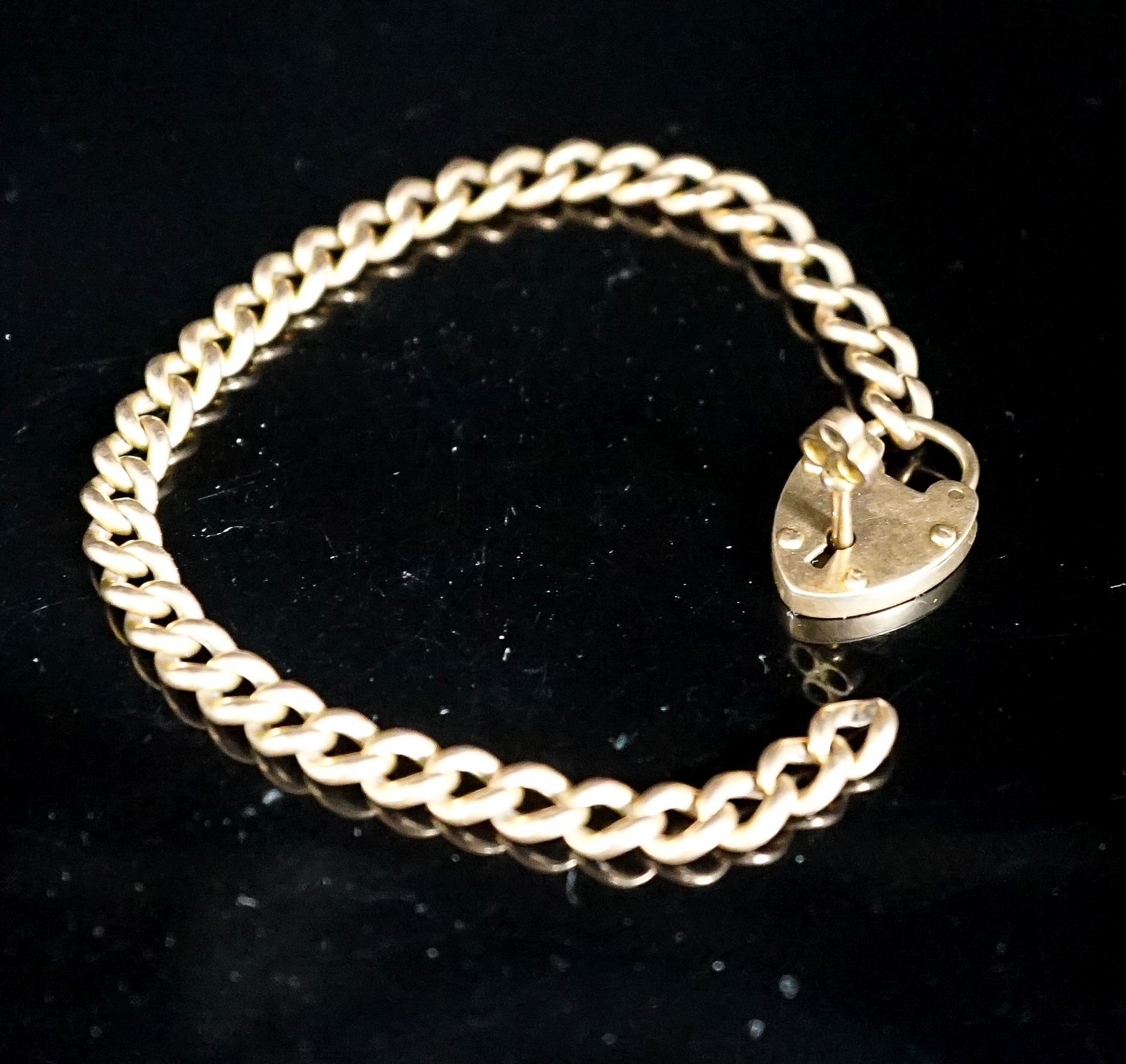 A yellow metal curb link bracelet with heart shaped clasp, with key, 20cm including clasp